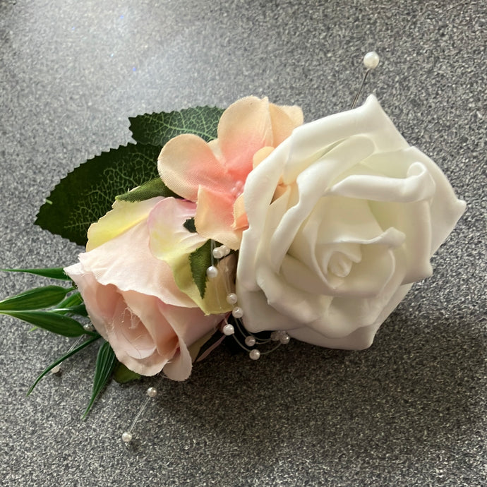 A corsage featuring blush pink and ivory roses