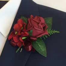 an artificial wedding buttonhole featuring a single burgundy foam rose