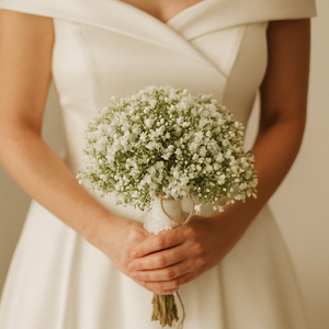 Person holding a bouquet of small white gypsophilia flowers in a neutral setting