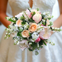 A wedding bouquet featuring silk peonies and roses in shades of pink and peach