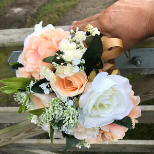 A wedding bouquet featuring silk flowers in shades of ivory and peach