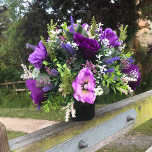 A purple and lilac memorial flower arrangement in black plastic pot