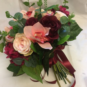 A brides bouquet featuring burgundy, peach & blush pink flowers