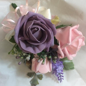 A Corsage featuring pale pink and lilac foam roses plus foliage