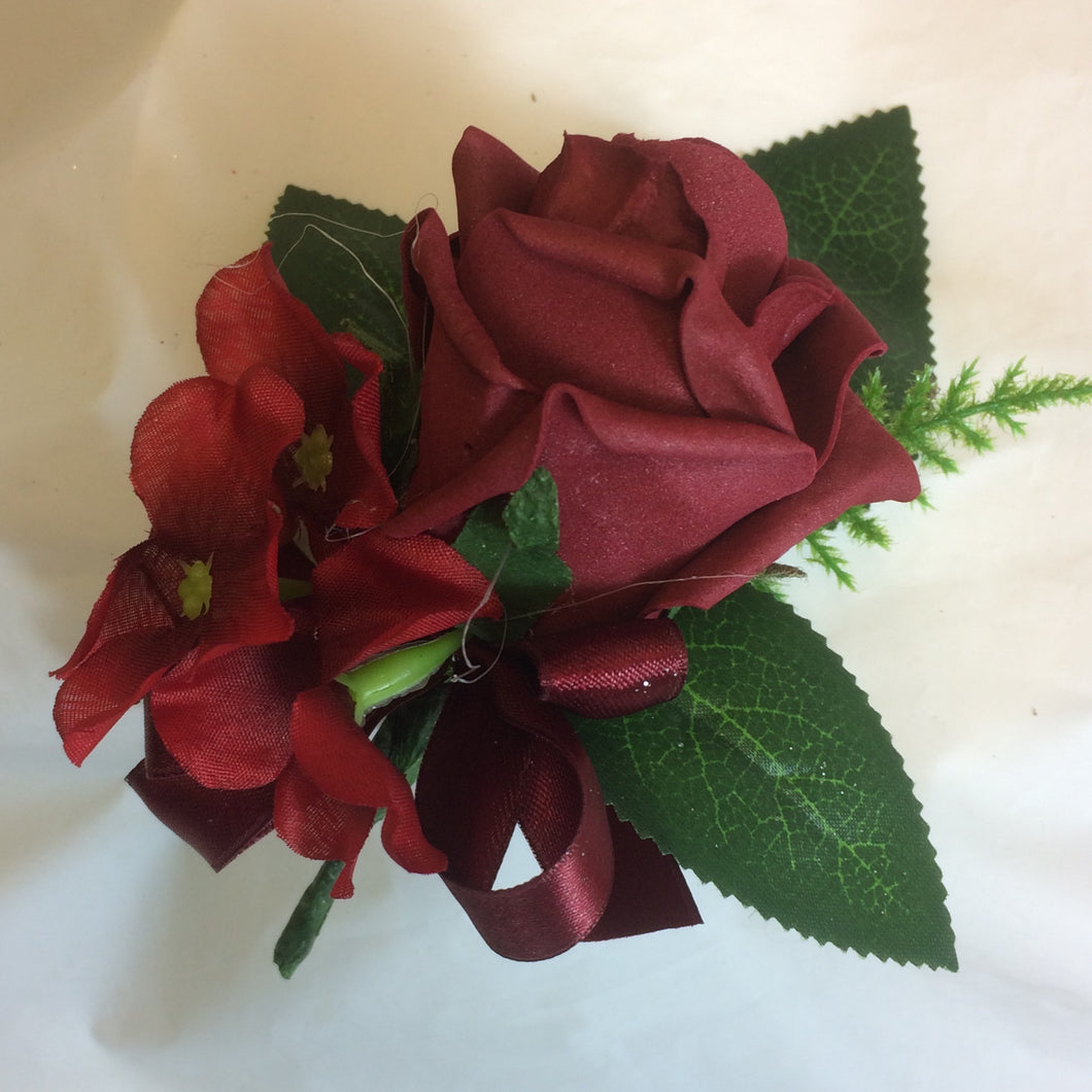 an artificial wedding buttonhole featuring a single burgundy foam rose