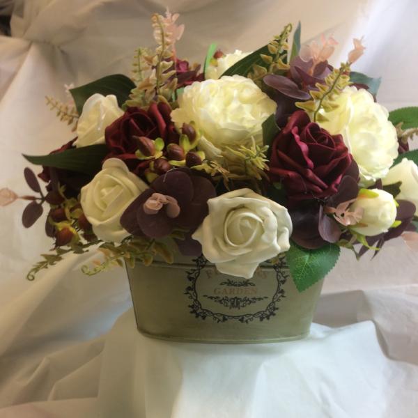 An artificial flower arrangement in shades of ivory and burgundy