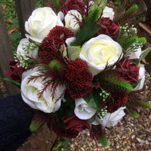 A wedding bouquet featuring ivory & burgundy roses, thistles & foliage