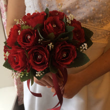 A brides wedding bouquet featuring artificial silk red roses