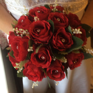 A brides wedding bouquet featuring artificial silk red roses