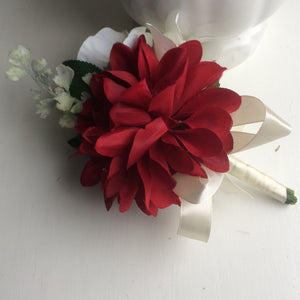 an artificial corsage featuring dahlia and roses in shades of burgundy & ivory