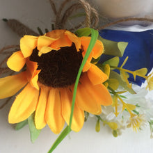 A corsage featuring a yellow sunflower & royal blue silk rose