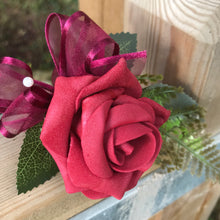 an artificial wedding buttonhole featuring a deep red/burgundy foam rose