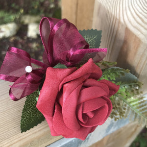 an artificial wedding buttonhole featuring a deep red/burgundy foam rose