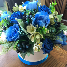 A flower arrangement of blue artificial flowers in hat box