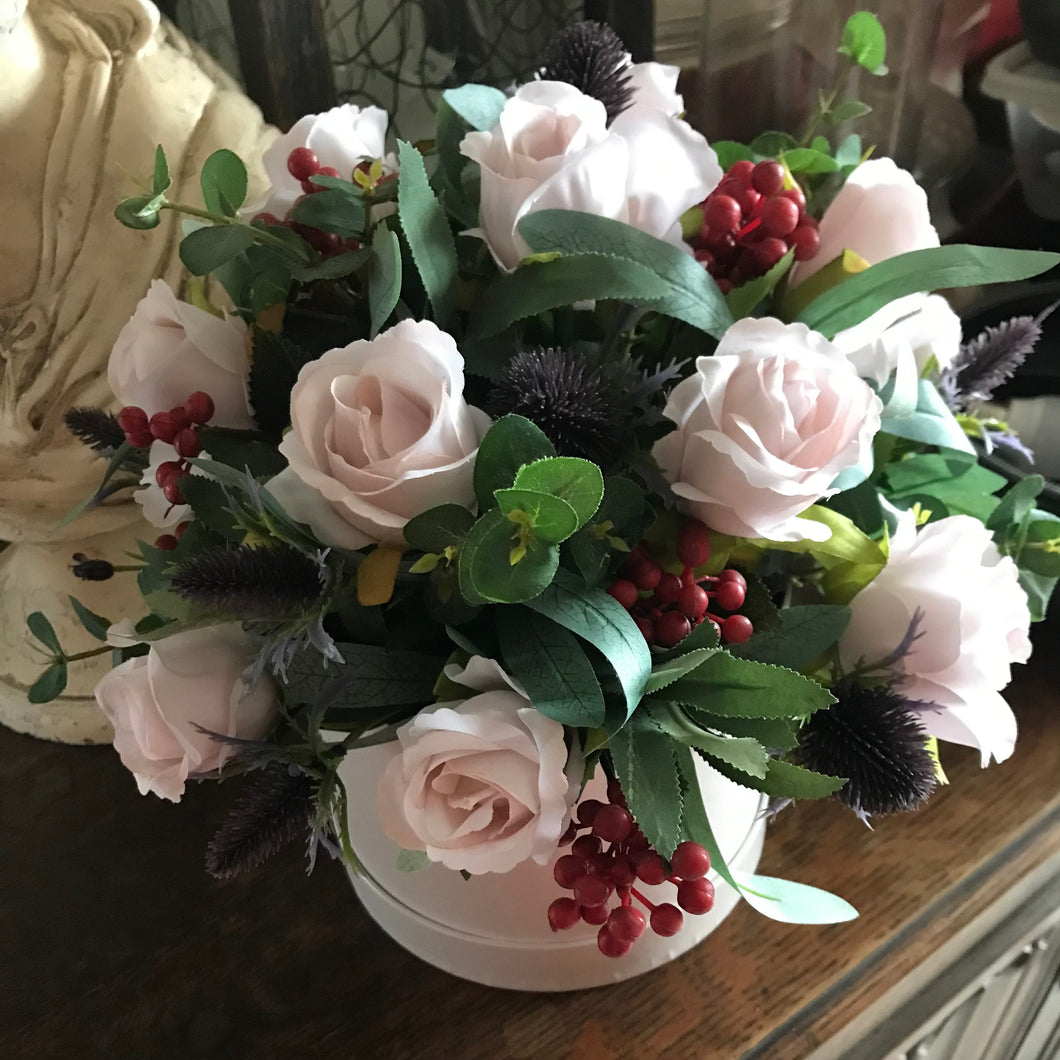 A flower arrangement of nude roses, thistles and berries in cream hat box