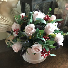 A flower arrangement of nude roses, thistles and berries in cream hat box
