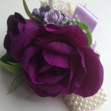 A wrist corsage featuring artificial purple & lilac roses & vintage lace bow