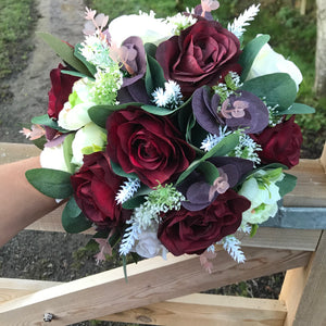 A brides bouquet of deep burgundy and ivory faux flowers