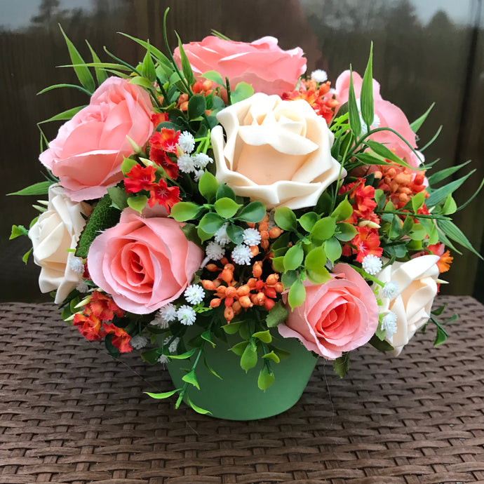 a flower arrangement of peach roses and foliage in a green ceramic pot