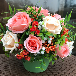 a flower arrangement of peach roses and foliage in a green ceramic pot