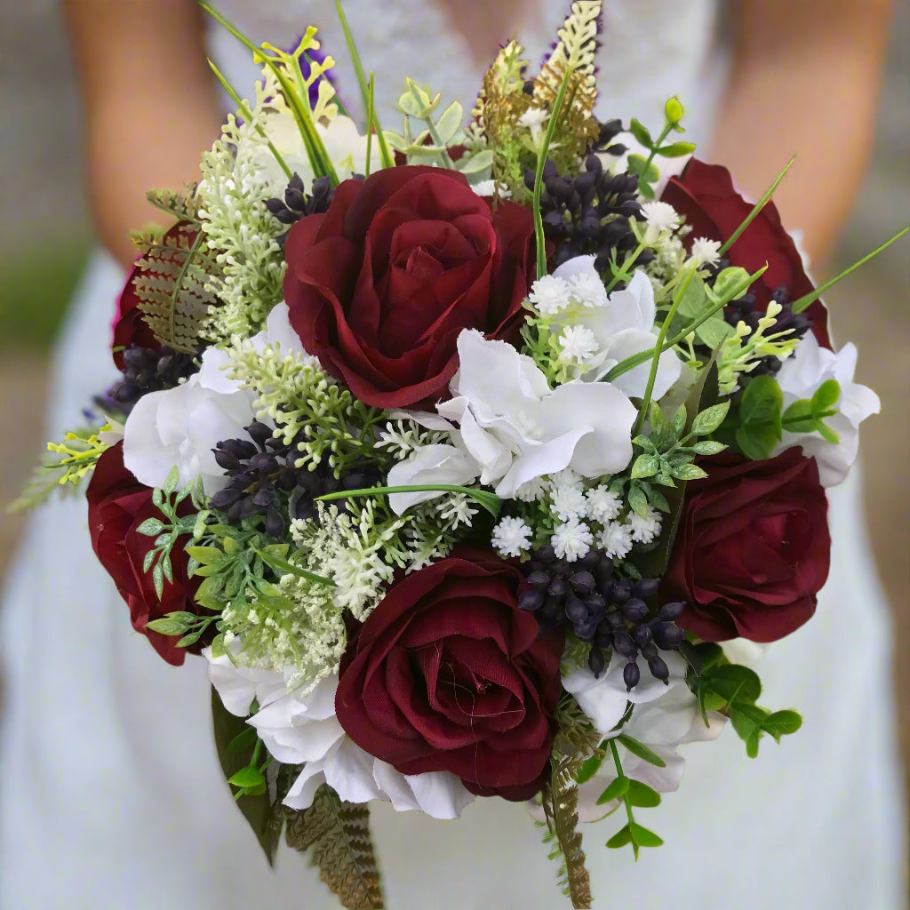 A wedding bouquet of artificial silk burgundy & ivory flowers, foliage & berries