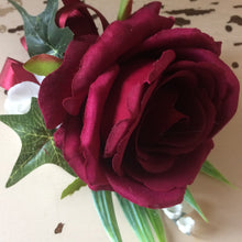 A buttonhole featuring a burgundy rose and lily of the valley