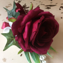 A buttonhole featuring a burgundy rose and lily of the valley