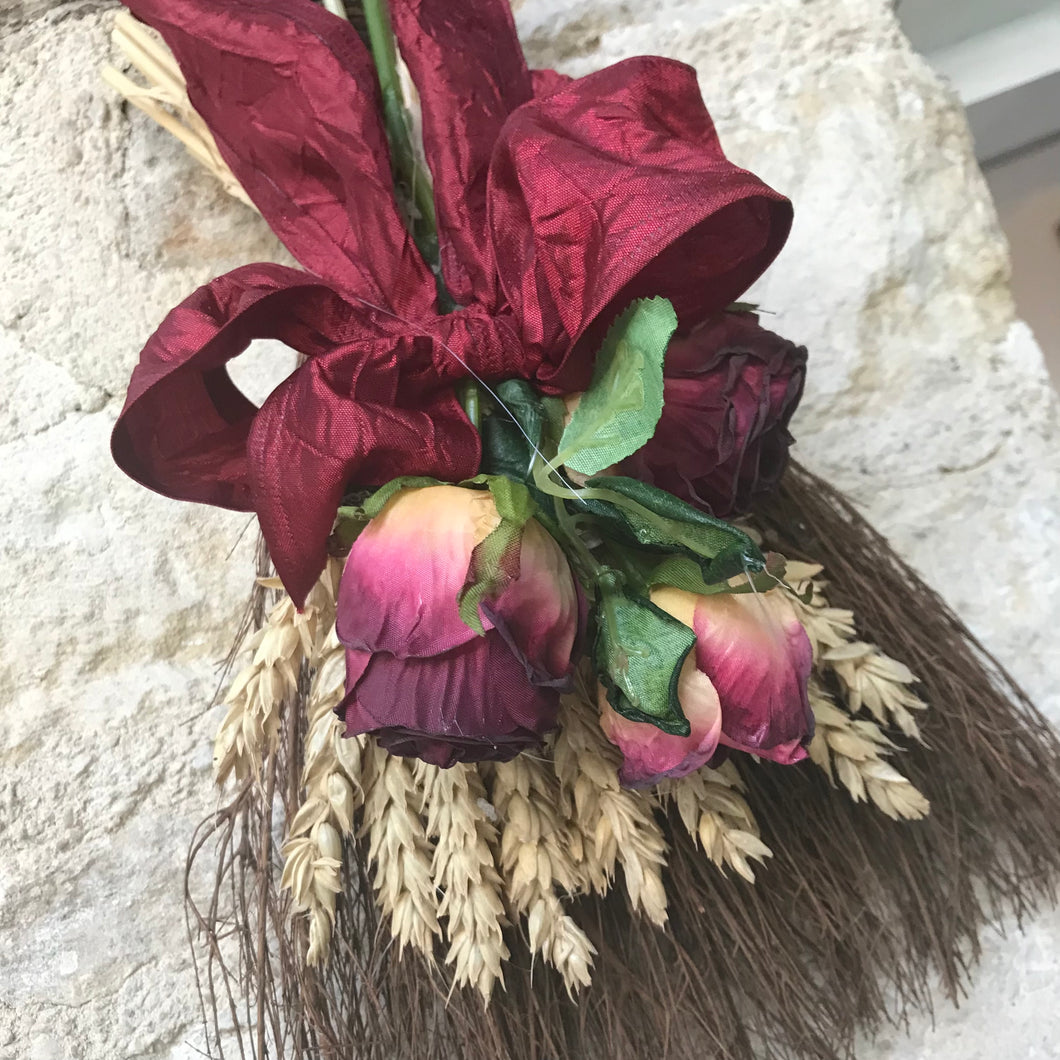 a twiggy broom decorated with burgundy dried look flowers
