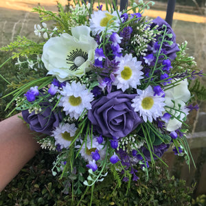 A wedding bouquet of artificial white, cream and deep lilac flowers