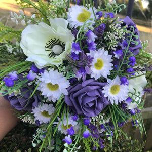 A wedding bouquet of artificial white, cream and deep lilac flowers