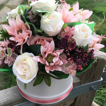 An arrangement of peach and burgundy flowers in cream hat box