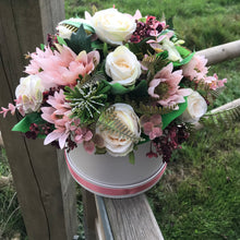 An arrangement of peach and burgundy flowers in cream hat box