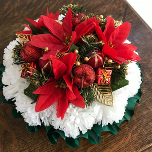 a memorial Christmas grave side posy of red poinsettia cones baubles and carnations