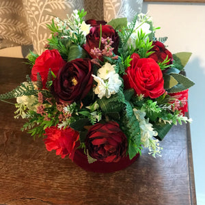 A flower arrangement of red artificial flowers in velvet hat box