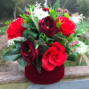 A flower arrangement of red artificial flowers in velvet hat box