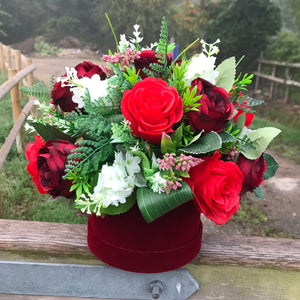 A flower arrangement of red artificial flowers in velvet hat box