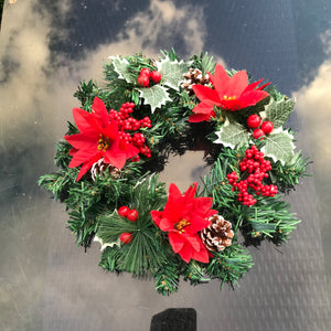 an artificial pine christmas wreath with holly and cones