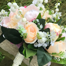 A wedding bouquet featuring silk peonies and roses in shades of pink and peach