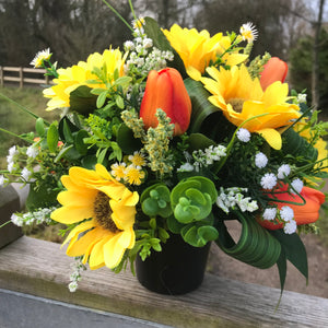 a grave side artificial silk flower arrangement in shades of yellow and orange