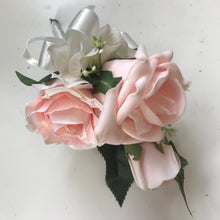 A corsage featuring blush pink artificial roses and foliage