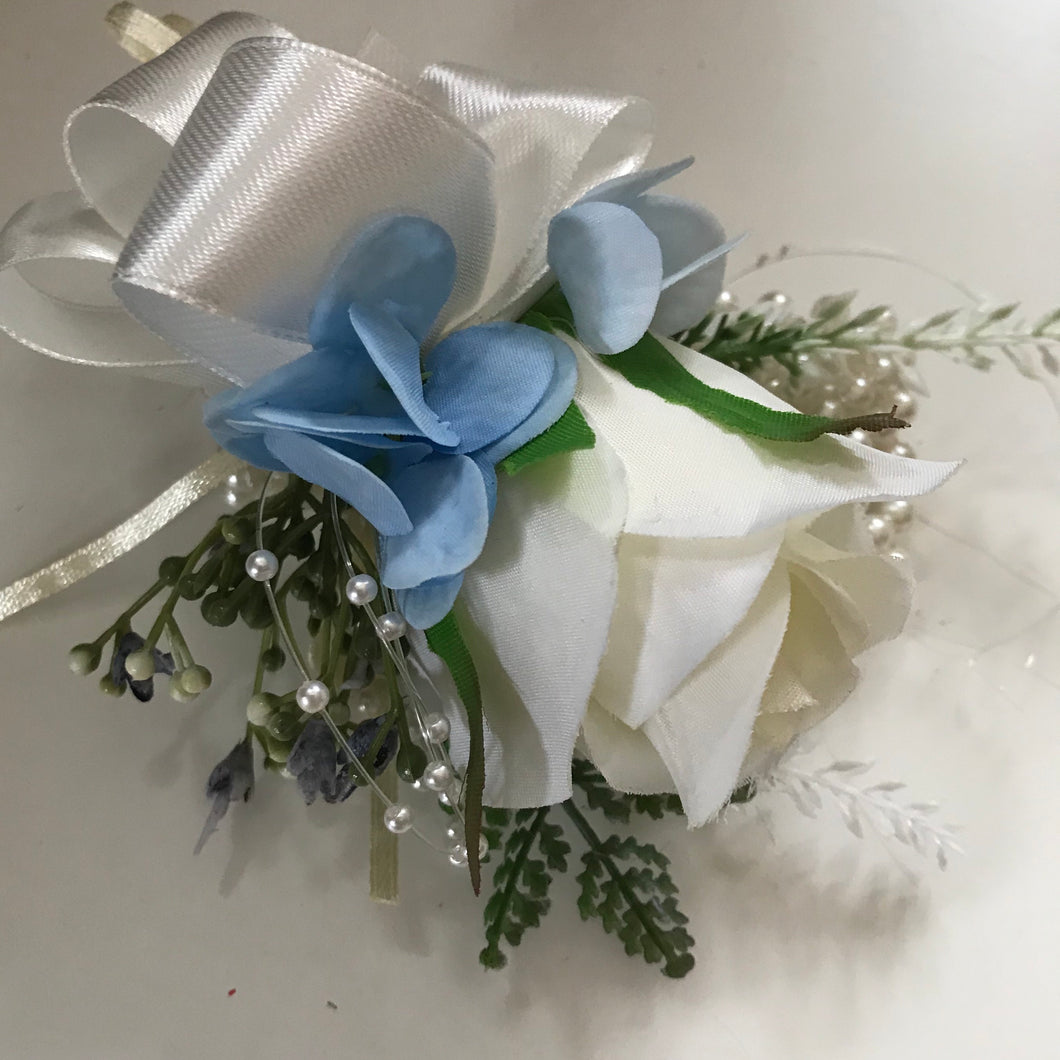 A wrist corsage featuring Ivory and blue flowers