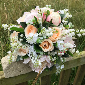 A wedding bouquet featuring silk peonies and roses in shades of pink and peach