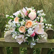 A wedding bouquet featuring silk peonies and roses in shades of pink and peach