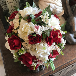 A brides bouquet featuring red and ivory artificial flowers