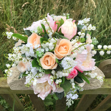 A wedding bouquet featuring silk peonies and roses in shades of pink and peach