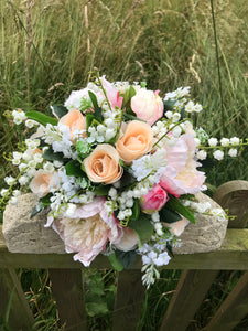 A wedding bouquet featuring silk peonies and roses in shades of pink and peach