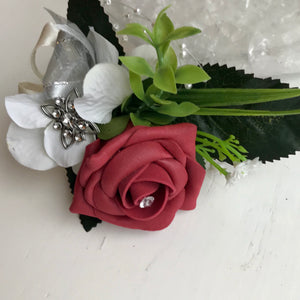 A flower corsage featuring burgundy foam roses and hydrangea