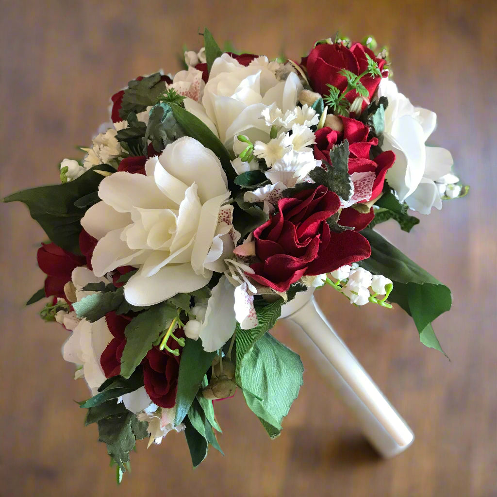 A brides bouquet featuring red and ivory artificial flowers