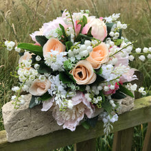 A wedding bouquet featuring silk peonies and roses in shades of pink and peach